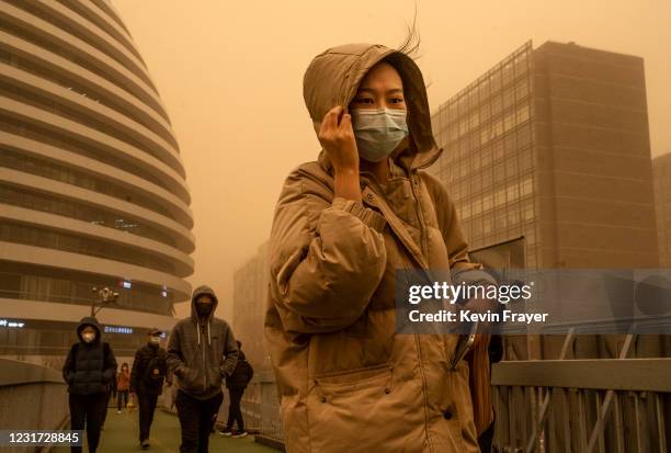 Woman wears a protective mask as she shields herself in heavy winds while commuting during a sandstorm on March 15, 2021 in Beijing, China. China's...