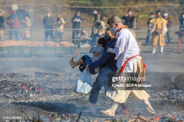 Monk helps a child and his grandmother to cross the field with embers of burning wood. The Fire Walking Festival is held near Mount Takao every...