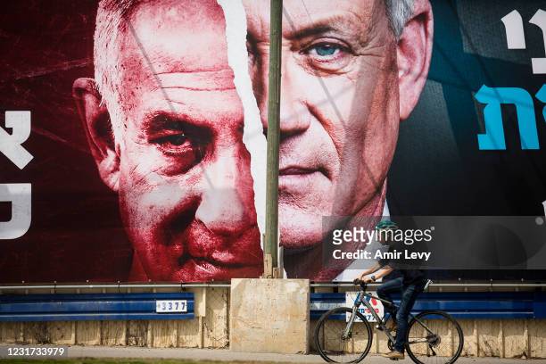 An Israeli man rides a bycicle by a Blue and White party campaign billboard showing Israeli Defence Minister Benny Gantz and Israeli Prime Minister...