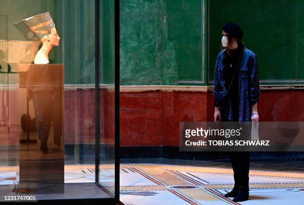 Visitor wearing a face mask looks at the Bust of Queen Nefertiti from Tell el-Amarna, the most famous exhibit at the Neues Museum with its collection...