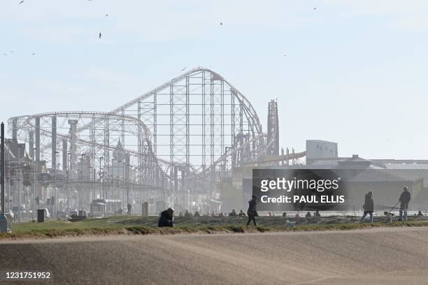 People enjoy the winter sunshine on the beach-front near the Blackpool Pleasure Beach amusement park in Blackpool, Lancashire on March 16 with the...