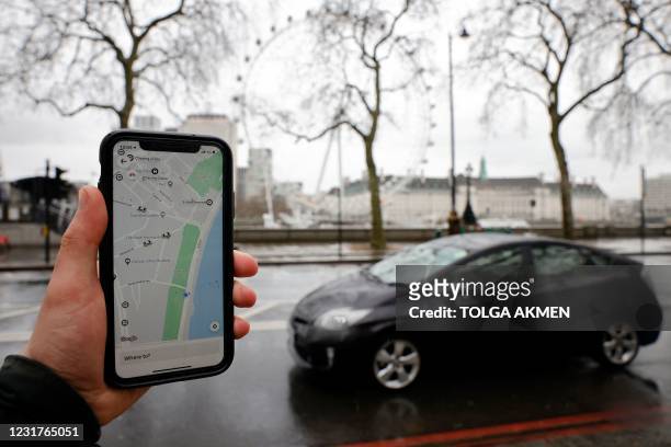 Man poses holding a smartphone showing the App for ride-sharing service Uber in London on March 17, 2021. - US ride-hailing giant Uber won praise...