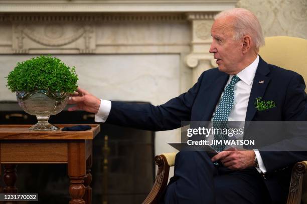 President Joe Biden looks at a bowl of shamrocks from Ireland, as he takes part in a virtual bilateral meeting with Irish Prime Minister Micheál...