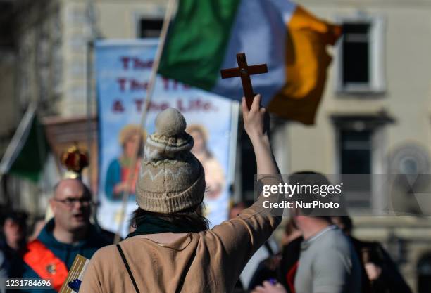 Woman carries a cross in front of many people take part in a religious procession through Dublin city center, with worshipers carrying a statue of...