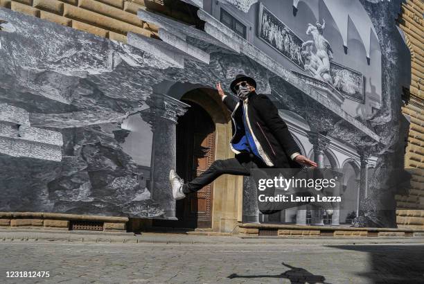 Artist JR jumps in the air in front of the facade of Palazzo Strozzi with his installation The Wound at Palazzo Strozzi on March 19, 2021 in...