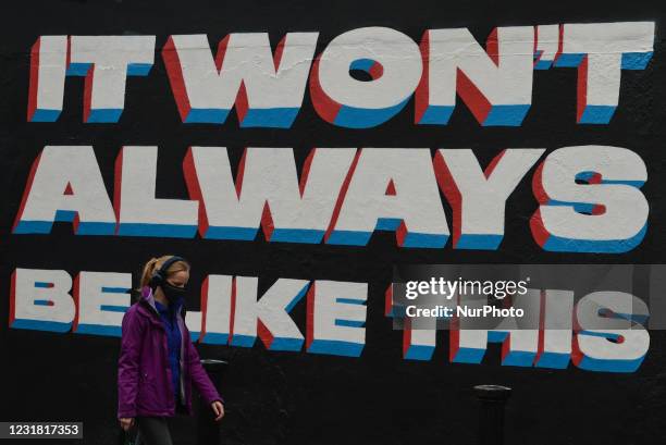 Woman wearing a face mask walks past a mural by Irish artist Emmalene Blake in Dublin's city centre during level 5 COVID-19 lockdown. The theme of...