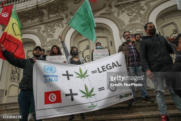 Protesters wave flags as they hold a banner with a drawing of cannabis leaf, handcuffs and the United Nations watermark, and that reads Legal, during...