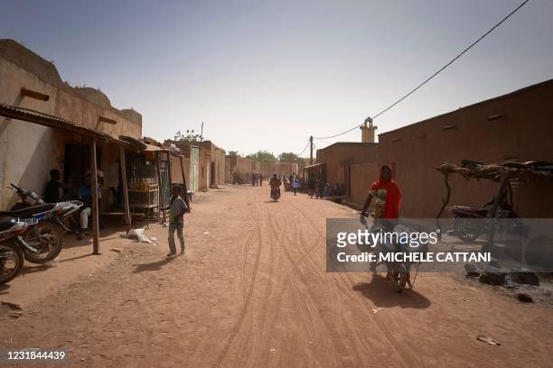 People walk along a main street in Konna on March 20, 2021 as the Malian Prime Minister and his delegation visit the town in central Mali to attend...