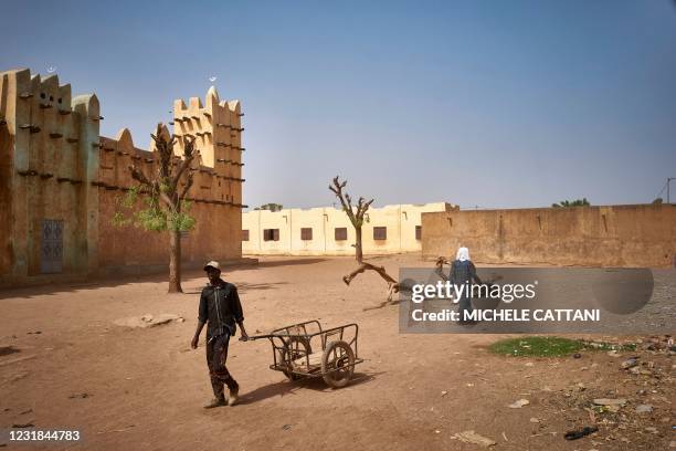 Men walk next to the great mosque of Konna on March 20, 2021 as the Malian Prime Minister and his delegation visit the town in central Mali to attend...