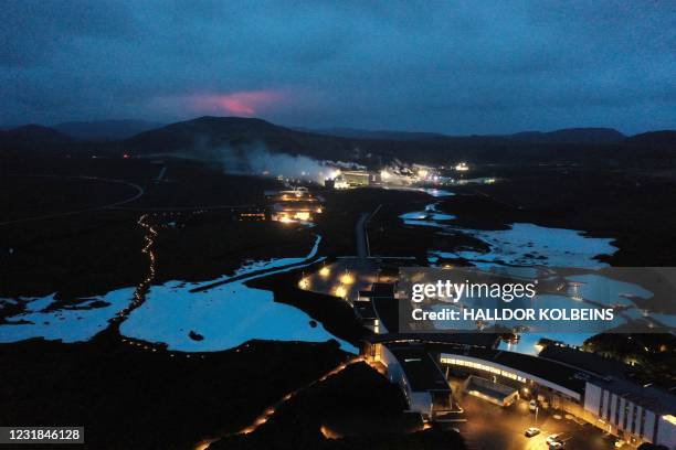 The red shimmer from magma is seen coming out from the erupting Fagradalsfjall volcano behind the tourist land mark Blue Lagoon, near the town of...