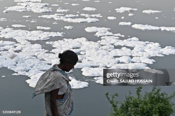 Woman is seen next to the river Yamuna half covered with foam due to pollution on the eve of 'World Water Day' in New Delhi on March 21, 2021.