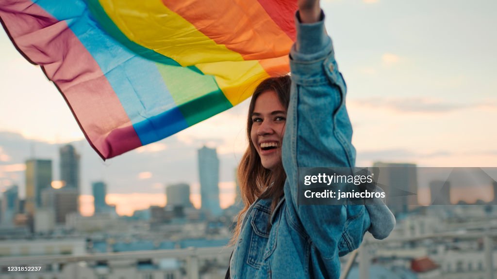LGBT proud. Happy woman holding lgbt flag. Rooftop view