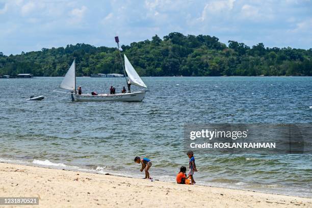 Children play on the beach as a boat sails past in the sea at Changi village in Singapore on March 22, 2021.