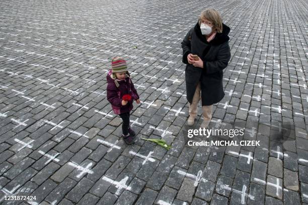 Woman and a girl arrive with flowers at the Old Town Square in Prague, on March 22 where thousands of crosses have been drawn onto the pavement to...