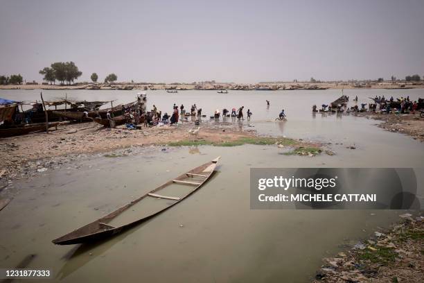 Broken pirogue is seen as people wash clothes and rams in the Bani river in Mopti on March 19, 2021. - Situated In the Inner Niger Delta region of...