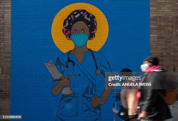 People walk past a mural by artist M. Tony Peralta picturing a healthcare worker at New York Presbyterian Hospital on March 22, 2021 in New York...