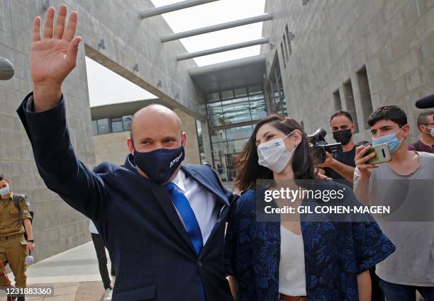 Israel's Naftali Bennett, leader of the right wing 'New Right' Yamina party, waves as he walks with his wife Gilat at a polling station where they...