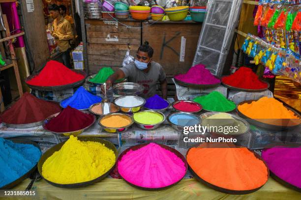 Shop owner wearing mask organizes various color powder or Gulal for sale ahead of Holi festival , at a market place in Kolkata , India , on 22 March...