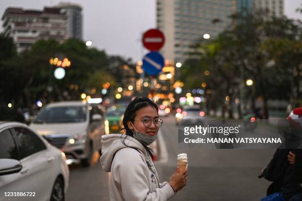 Girl carrying ice-cream cones waits to cross a street in Hanoi on March 23, 2021.