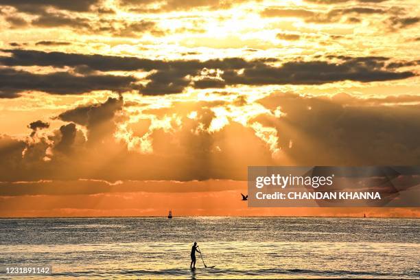 Man paddleboards during a sunrise on the beach in Miami Beach, Florida, on March 23, 2021.