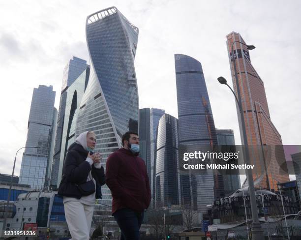 People wearing face mask to protect against the coronavirus walk along the embankment in front of skyscrapers of the Moscow International Business...