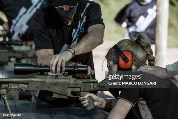 Technician and a fire range officer hold the shooting position of a gun enthusiast as she squeezes the trigger of a South African made Truvelo .308...