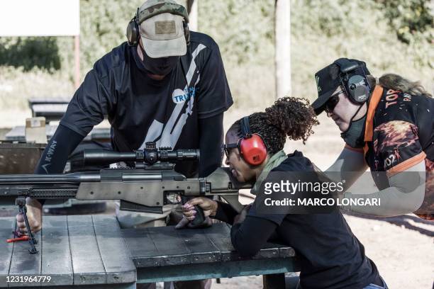 Technician and a fire range officer hold the shooting position of a gun enthusiast as she squeezes the trigger of a South African made Truvelo...