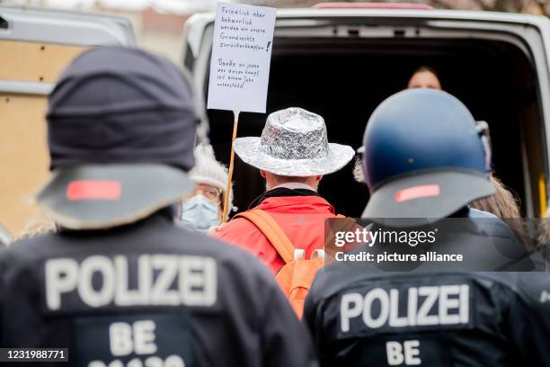 March 2021, Berlin: A man wearing an aluhut stands behind police officers during a demonstration against the Corona measures at Rosa-Luxemburg-Platz....