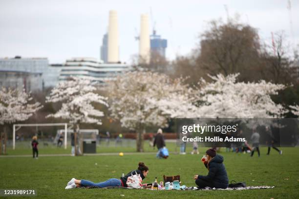 People sit in Battersea Park on March 28, 2021 in London, England. Starting tomorrow, England will ease its rules on socialising and recreation, with...