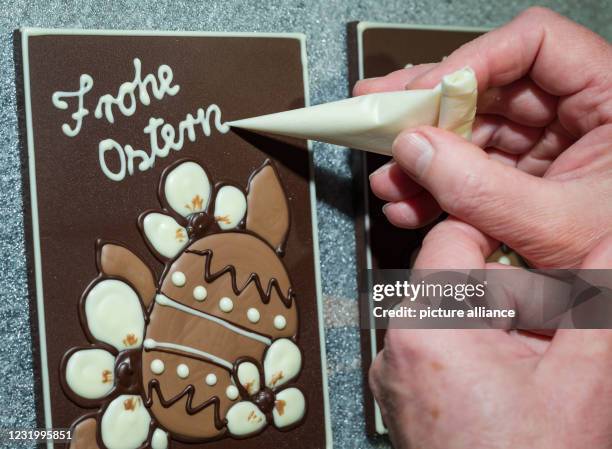 March 2021, Brandenburg, Hornow: An employee of Confiserie Felicitas GmbH uses liquid chocolate to write "Happy Easter" on a chocolate bar. Chocolate...