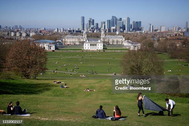 Pedestrians relax in Greenwich Park in view of Greenwich Maritime Institute and skyscrapers in the Canary Wharf business, finance and shopping...