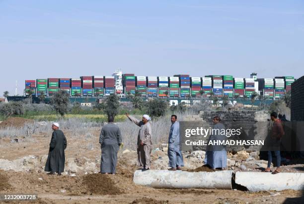 People watch the Panama-flagged MV 'Ever Given' container ship as it is tugged in Egypt's Suez Canal after it was fully dislodged from the banks,...