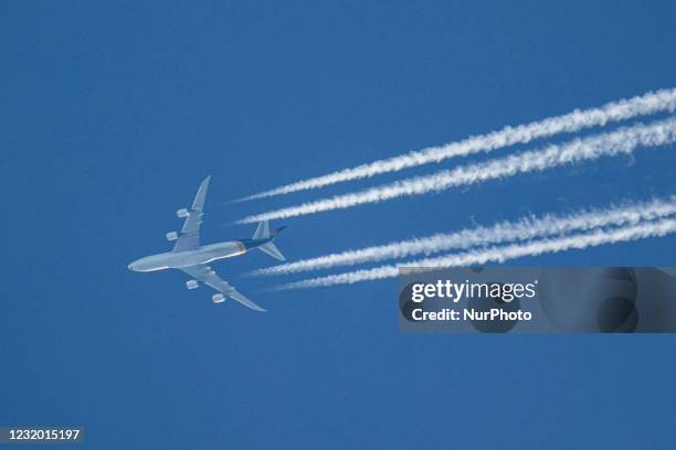 Boeing 747-8F aircraft as seen flying in the blue sky over the Netherlands. The overflying Jumbo Jet airplane is cruising at high altitude leaving...