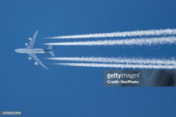 Boeing 747-8F aircraft as seen flying in the blue sky over the Netherlands. The overflying Jumbo Jet airplane is cruising at high altitude leaving...