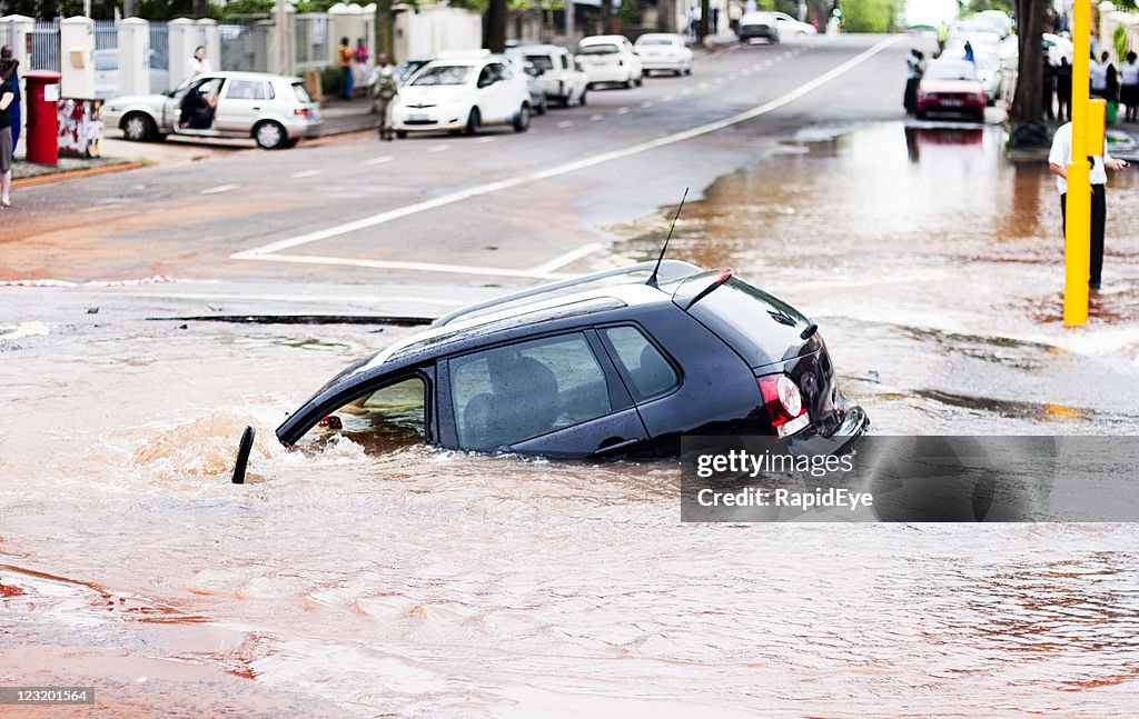 Car tips into pothole in flooded street, side view