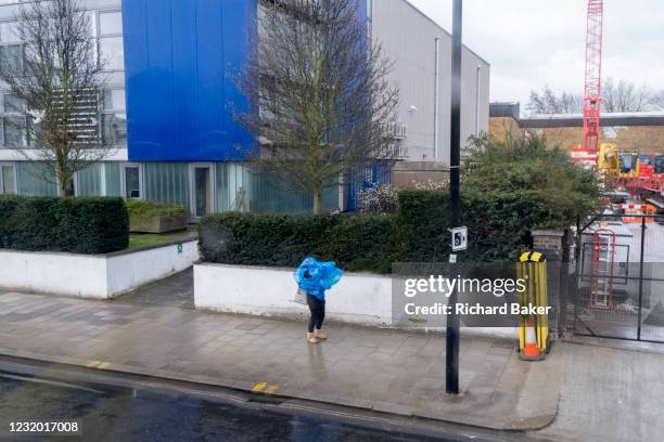 Person pauses outside business premises with a blue exterior, to put on a blue plastic cagoule 'poncho' over their head in a Brixton street, on 15th...