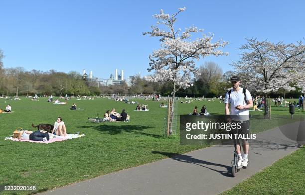 Man rides a scooter as people enjoy the sunshine in Battersea Park, central London on March 30 as England's third Covid-19 lockdown restrictions...