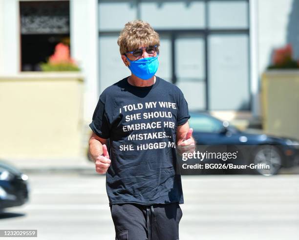 Howie Mandel is seen wearing a wig, sunglasses and a t-shirt with a joke printed on it reading "I told my wife should embrace her mistakes. She...