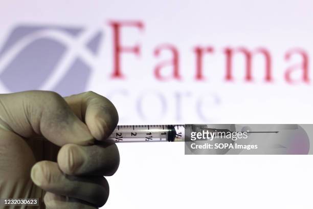 In this photo illustration, a medical syringe held with the Farmacore Biotecnologia company logo displayed on a screen in the background.