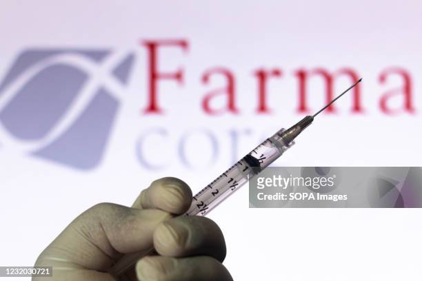 In this photo illustration, a medical syringe held with the Farmacore Biotecnologia company logo displayed on a screen in the background.