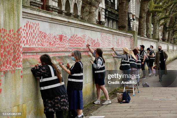 People paint red hearts representing the 150,000 victims who have died of the coronavirus , on the National Covid Memorial Wall, opposite the Houses...