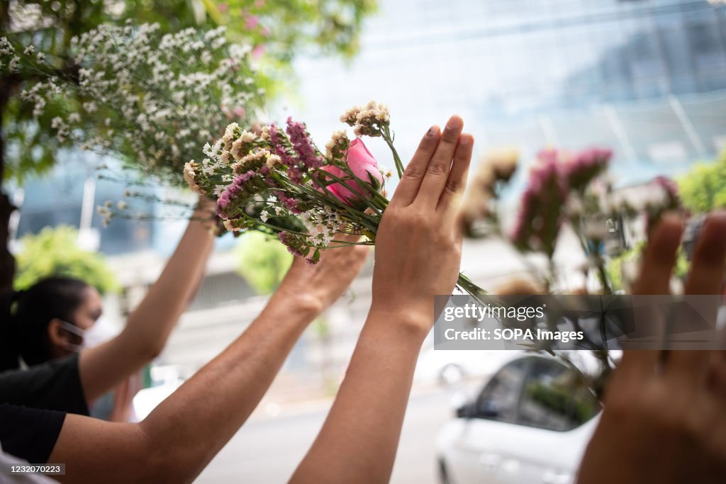 People make three-finger salutes while holding flowers in...