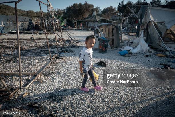 Refugee girl playing in the ashes of the ruined from the fire camp. Close up of underaged, minors asylum seekers who live with their families around...