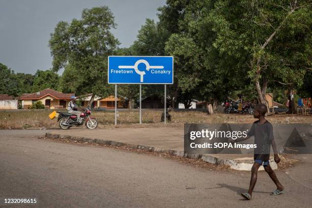 Boy walks past a signpost that points to both Sierra Leone capital Freetown and Guinea's capital Conakry. The latest Ebola outbreak in Guinea was...