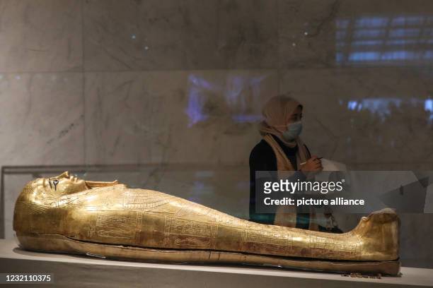 April 2021, Egypt, Cairo: A visitor stands next a golden sarcophagus displayed at the National Museum of Egyptian Civilisation , in the Fustat...