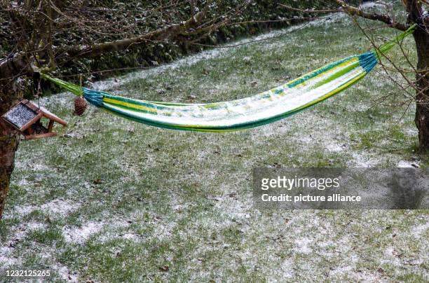 April 2021, Mecklenburg-Western Pomerania, Pokrent: Snow and sleet lie in a hammock in a garden. With cool temperatures, strong winds and snow...