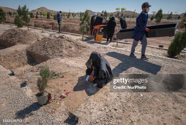 An Iranian cemetery worker in a protective suit carrying a coffin as a family of a man who has died from coronavirus disease, stand next to his grave...