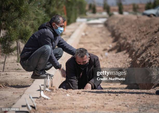 Iranian men wearing protective face masks mourn as they sit next to the grave of their father who has died from coronavirus disease, in the...