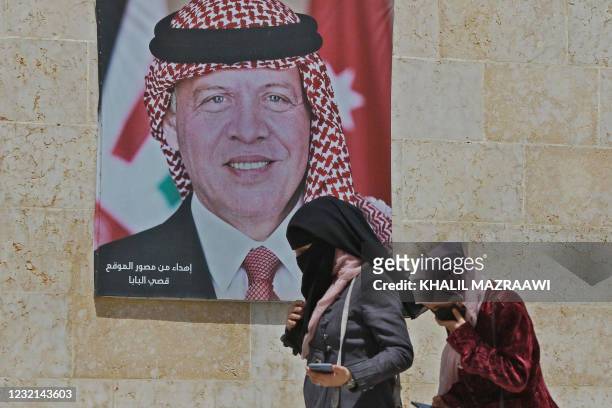 Women walk past a poster of Jordan's King Abdullah II on a street in the capital Amman, on April 6 after a security crackdown revealed tensions in...