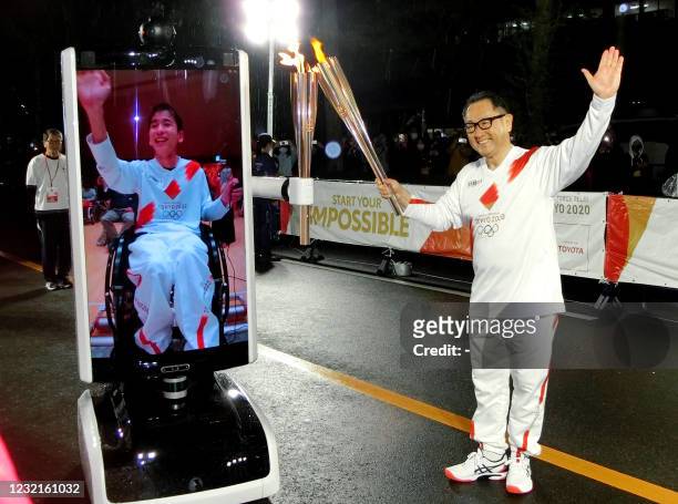 In this photograph taken on April 6, 2021 Toyota Motor Corp. President Akio Toyoda passes the olympic flame to Japanese disabled Shunsuke Suzuki via...